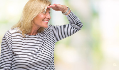 Middle age blonde woman over isolated background very happy and smiling looking far away with hand...