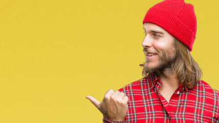Young handsome man with long hair wearing red cap over isolated background smiling with happy face looking and pointing to the side with thumb up.