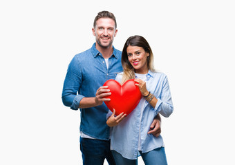 Young couple in love holding red heart over isolated background with a happy face standing and smiling with a confident smile showing teeth