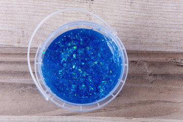 Blue glitter slime in a plastic bucket on a wooden table