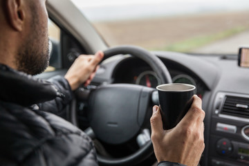 the driver in the car holds a drink cup in his hand