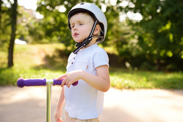 Toddler boy in safety helmet learning to ride scooter