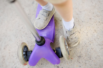 Toddler boy learning to ride scooter. Feet close up.