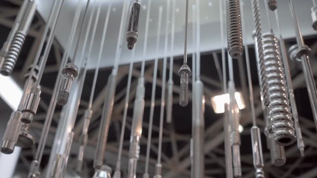 Various bolts, metal studs with thread and other metal parts from the equipment are hang and shine in the light. Shot in motion