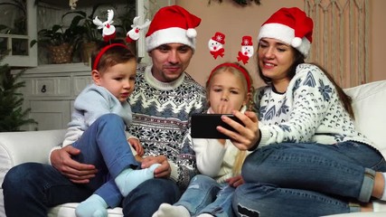 Happy lovely two kids family spending time together watching cartoons on smart device in Christmas tree decorated room