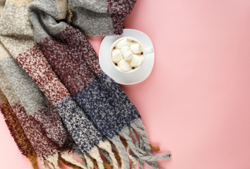 Warm, cozy winter clothing, scarf and cup of coffee with white marshmallow as frame on pastel  pink background. Christmas concept flat lay. 
