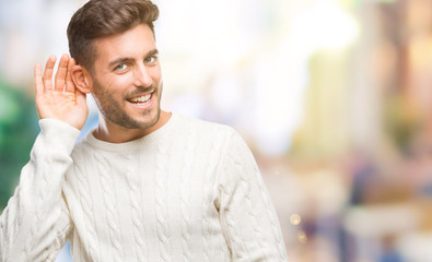Naklejka premium Young handsome man wearing winter sweater over isolated background smiling with hand over ear listening an hearing to rumor or gossip. Deafness concept.