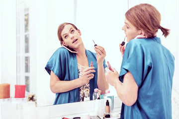 Transgender woman putting on makeup in mirror while holding phone