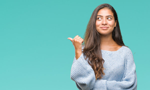 Young beautiful arab woman wearing winter sweater over isolated background smiling with happy face looking and pointing to the side with thumb up.