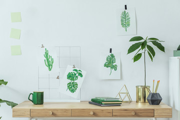 Stylish and modern scandinavian home office desk with alot of floral graphics, avocado plant,cup of coffee and office accessories. Modern composition of home office desk.