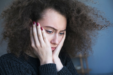 Close up of teenager with depression and bulimia sitting alone in dark room. She covers her face with hands. Mental problems with depression and bulimia.