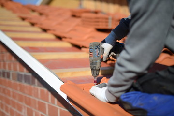 Dachdecker Handwerker schraubt roten Dachziegel am Dachrand mit Akkuschrauber fest