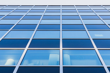 The facade of a glass building. The windows are blue and dark blue. Steel horizontal and vertical lines between the windows.