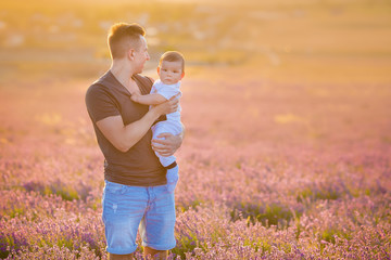 Fototapeta premium Family portrait of father holding baby son posing on lavender field wearing blue jeans and t-shirt.