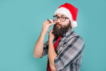 Bearded man in Santa Claus hat shaves standing on blue background