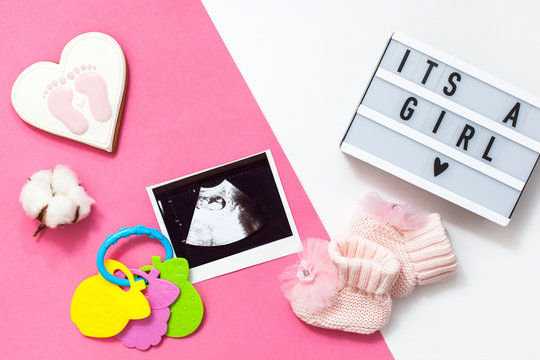 flatlay pregnancy composition with space for text on white and pink background. top view of children's accessories: toys, pacifier, baby screen, baby projector lamp "it's a girl", a cotton flower 