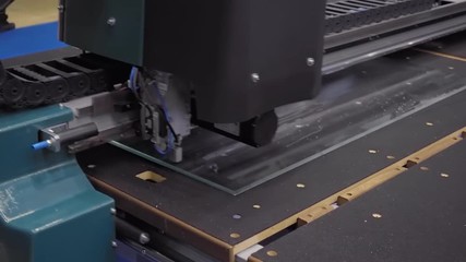 An industrial glass cutting machine cuts a piece of glass and the operator breaks it down on the cutting line