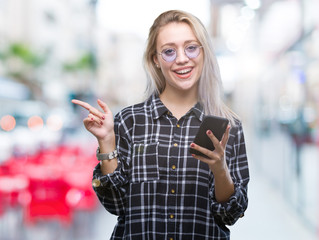 Young blonde woman texting sending message using smartphone over isolated background very happy pointing with hand and finger to the side