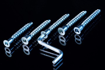 Powerful screws and key for the repair of equipment on a black background. Screw-a fastener for connecting parts, has the form of a rod with an external thread and a head adapted for screwing with a s