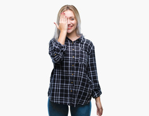 Young blonde woman over isolated background covering one eye with hand with confident smile on face and surprise emotion.