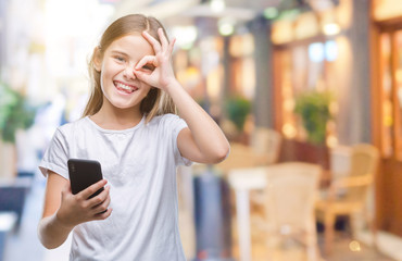 Young beautiful girl sending message texting using smarpthone over isolated background with happy face smiling doing ok sign with hand on eye looking through fingers