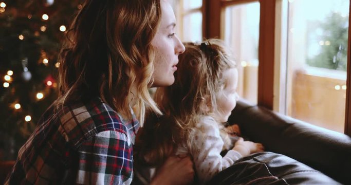 Mother and Daughter Having Fun on Christmas Morning. SLOW MOTION. Precious family moment, young mom playing with her toddler daughter by the window, winter landscape. 