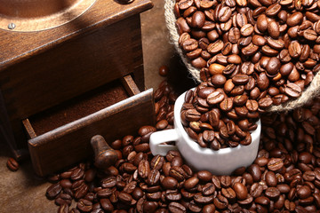 Fresh roasted coffee beans in burlap sack, coffee cup and grinder on dark background.