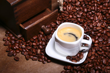 Fresh roasted coffee beans in burlap sack, coffee cup and grinder on dark background.