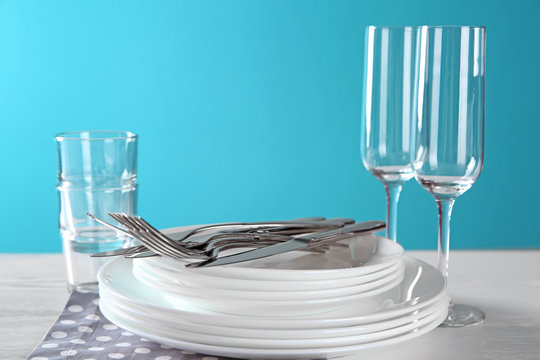 Set of clean dishes, glasses and cutlery on table against color background