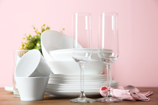 Set of clean dishes and glasses on table against color background