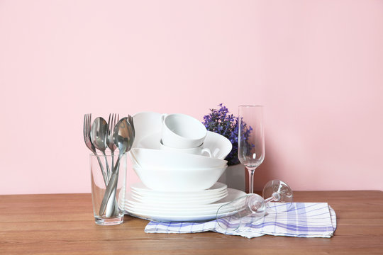 Set of clean dishes and cutlery on table against color background