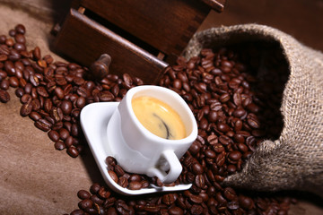 Fresh roasted coffee beans in burlap sack, coffee cup and grinder on dark background.