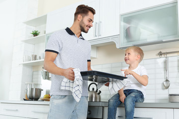 Young man and his son with oven sheet in kitchen