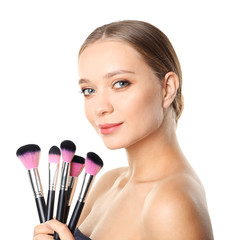 Portrait of beautiful young woman with makeup brushes on white background