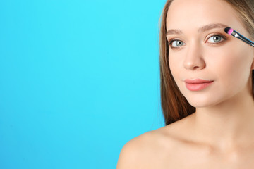 Fototapeta premium Portrait of beautiful young woman with makeup brush on color background. Space for text
