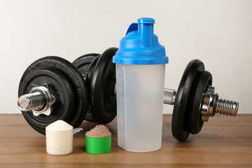 Fototapeta na wymiar Empty protein shake sport bottle, scoops with powders and dumbbells on table