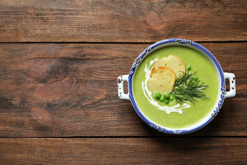 Fresh vegetable detox soup made of green peas with croutons in dish and space for text on wooden background, top view