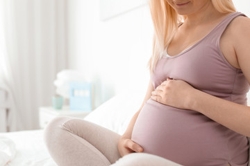 Pregnant woman sitting on bed in light room. Space for text