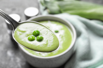 Spoon with fresh vegetable detox soup made of green peas on blurred background, closeup