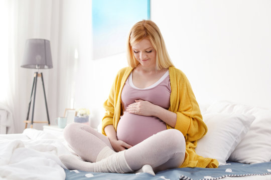 Beautiful pregnant woman sitting on bed in light room