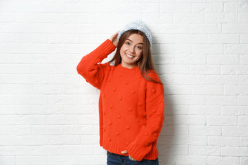Obraz na płótnie Canvas Beautiful young woman in warm sweater with hat near white brick wall
