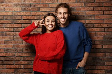 Fototapeta na wymiar Young couple in warm sweaters near brick wall