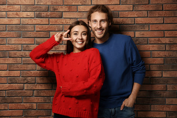 Young couple in warm sweaters near brick wall