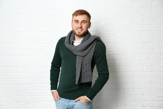 Handsome young man in warm sweater with scarf near white brick wall