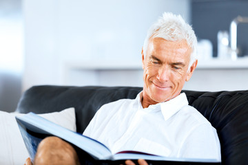 Fototapeta na wymiar Handsome sennior man reading a book relaxing on a sofa