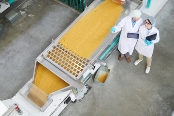 Top view  portrait of two female factory workers standing by macaroni conveyor belt during quality...