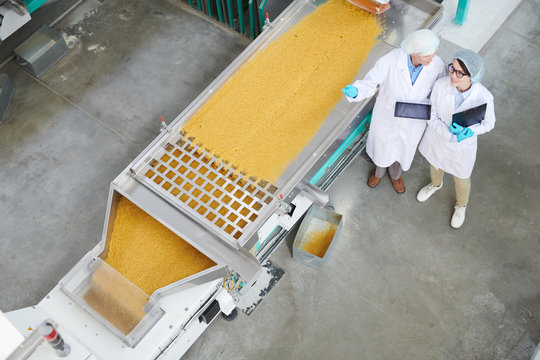 Top View  Portrait Of Two Female Factory Workers Standing By Macaroni Conveyor Belt During Quality Inspection At Food Production , Copy Space