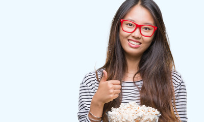 Young asian woman eating popcorn over isolated background happy with big smile doing ok sign, thumb up with fingers, excellent sign