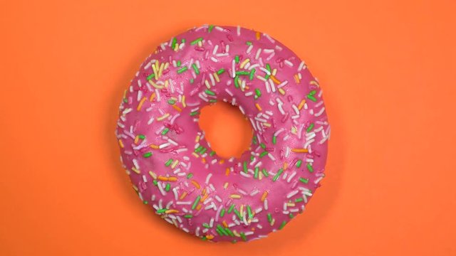 Tasty and fresh sprinkled donut close-up macro shot spinning on a orange background.