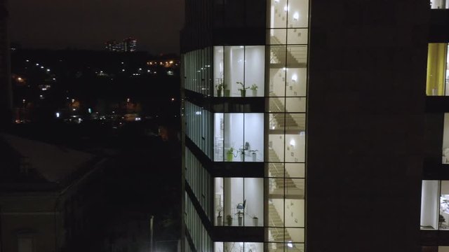 Aerial view of a modern glassed office building exterior with glowing windows at night